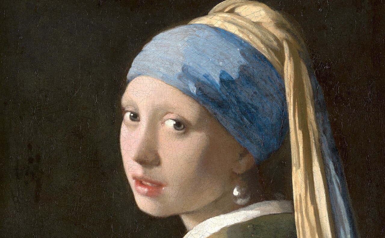 Girl with a Pearl Earring, Johannes Vermeer, about 1665, detail: a girl in a blue and yellow turban turns her head over her shoulder towards the viewer, lips parted, a large pearl at her ear, against a dark background